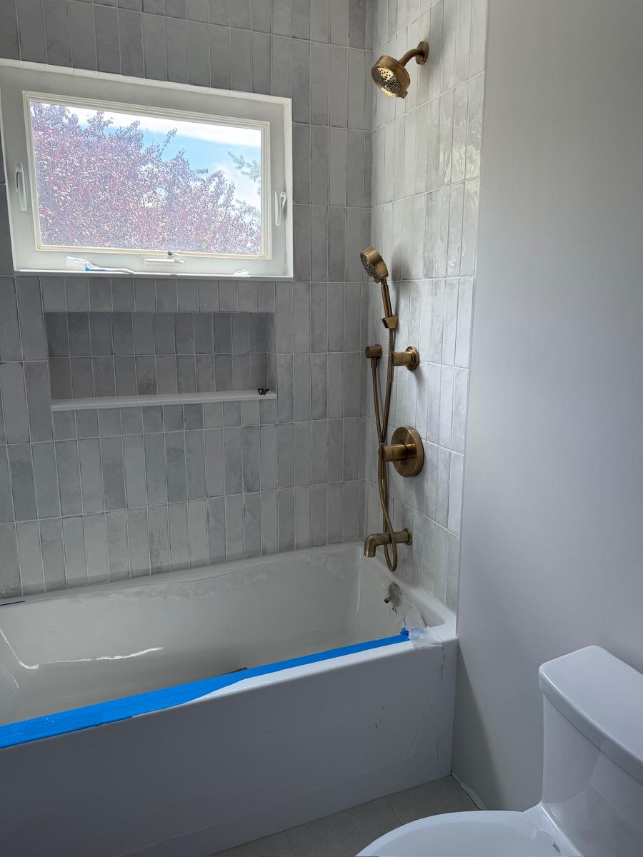 Bathtub with brass fixtures and tile surround near completion