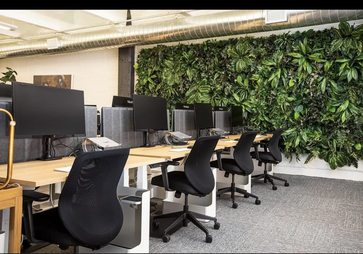 Modern commercial office with communal workstations, exposed ductwork, and living plant wall