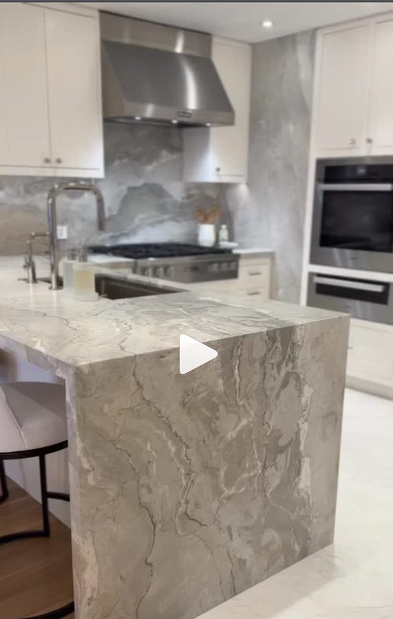 Luxury kitchen with marble waterfall island, stainless appliances, and white shaker cabinets