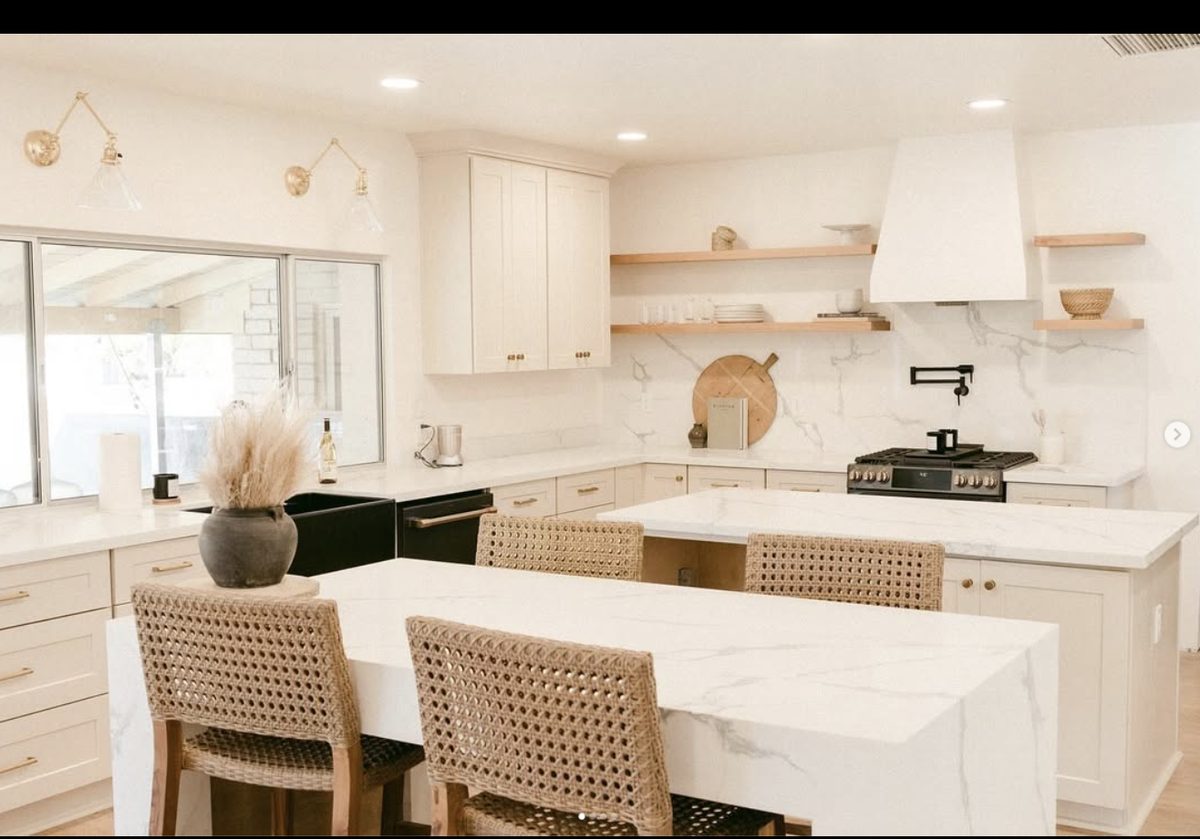 White kitchen with marble quartz waterfall island, floating wood shelves, and black farmhouse sink